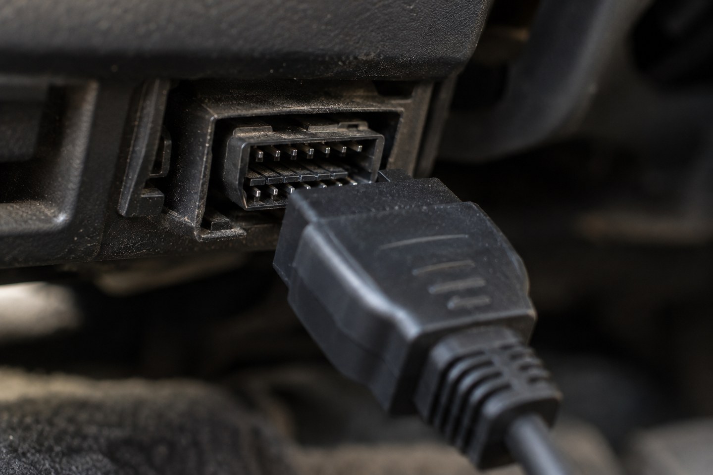Prise de diagnostic OBD sous le tableau de bord d'une voiture, avec sa fiche noire en cours de branchement