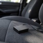 Traceur GPS voiture : comment choisir sans se tromper Petit boîtier électronique noir relié à un câble, posé sur la banquette avant d'une voiture